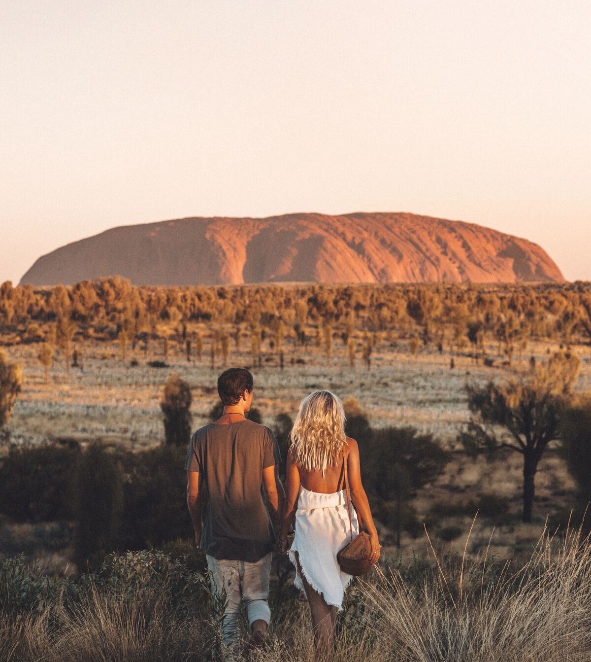 two people walking in the outback with Ayers Rock in the distance